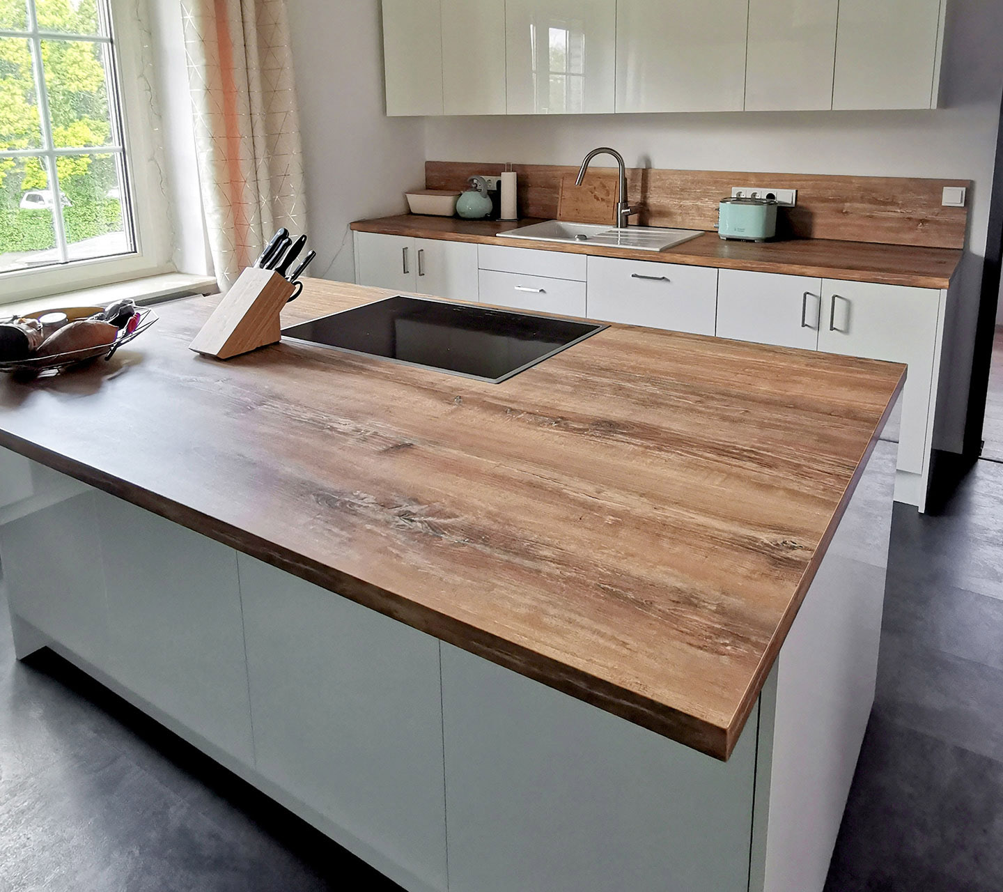 Küche mit großer Kücheninsel. Hochglanzfronten im Kontrast zur Holzdekor-Arbeitsplatte, grifflos ausgeführte Oberschränke